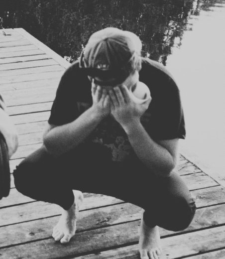 Logan F. crouched on a dock with his head in his hands.
