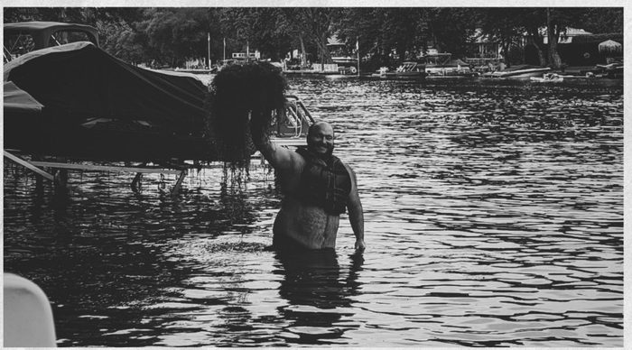 Mr Mud rising from the lake holding a fistful of weeds.