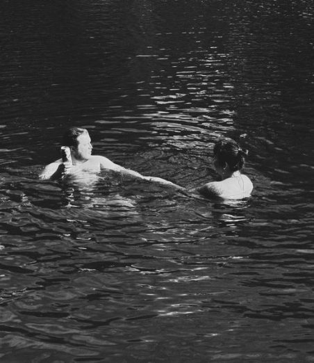 Two figures in dark water at night, one holding a drink.
