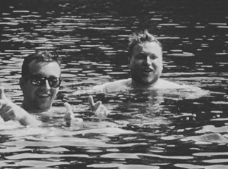 Two men in the lake, one giving a peace sign.